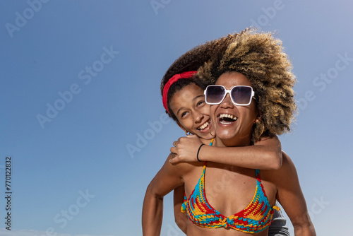 An adult and a child share a joyous hug and laughter against a clear blue sky on a sunny beach day, showcasing warmth and happiness photo