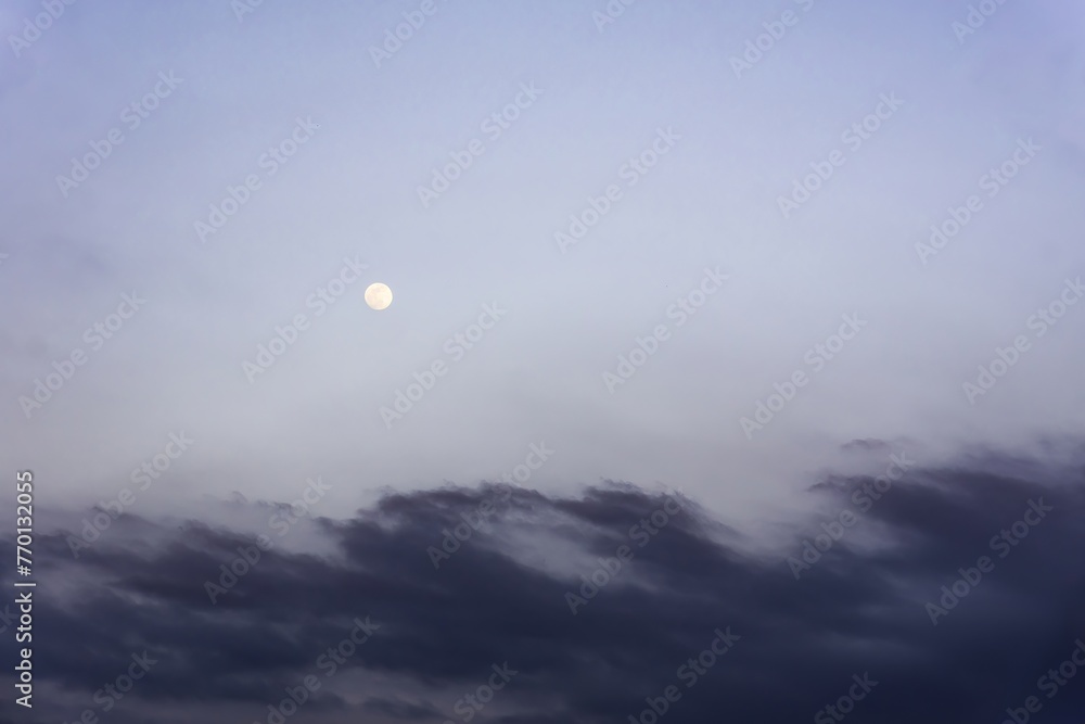Full moon peeking through the clouds. Bluish sky at dusk. Backgrounds. Copy space. Full moon peeking through the clouds. Bluish sky at dusk. Backgrounds. Copy space.