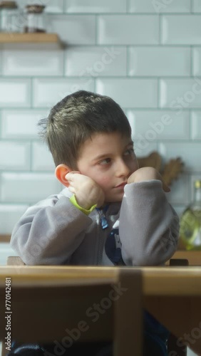 Vertical video. Little upset kid sitting in kitchen alone at home. Lonely offended schoolboy feeling disappointed bullied, stressed sit at table. School children problem	
