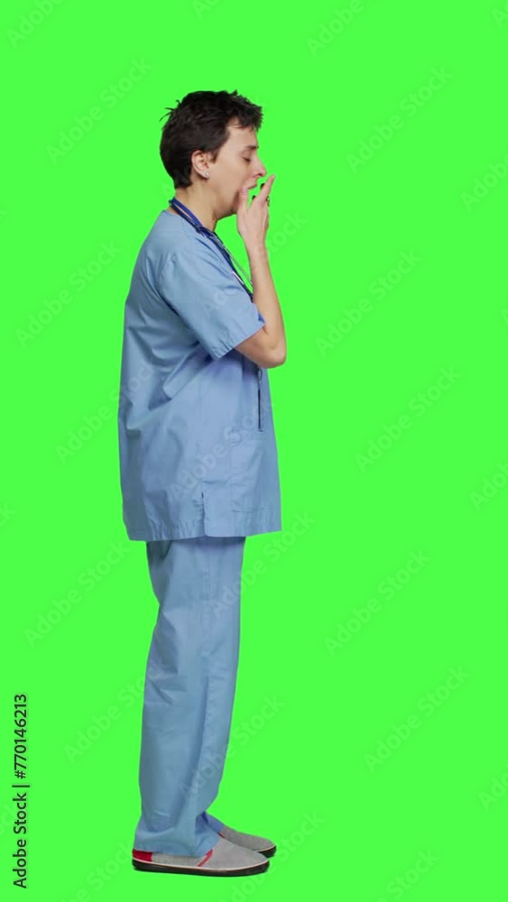 Profile Medical assistant feeling extremely sleepy against greenscreen backdrop, being overworked after the night shift. Woman nurse yawns and feels exhausted in studio, burnout and anxiety. Camera A. Profile Medical assistant feeling extremely sleepy against greenscreen backdrop, being overworked after the night shift. Woman nurse yawns and feels exhausted in studio, burnout and anxiety. Camera A.