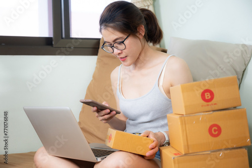 Young Asian woman checking customer order from online shopping and prepare paper boxes parcel for delivery.