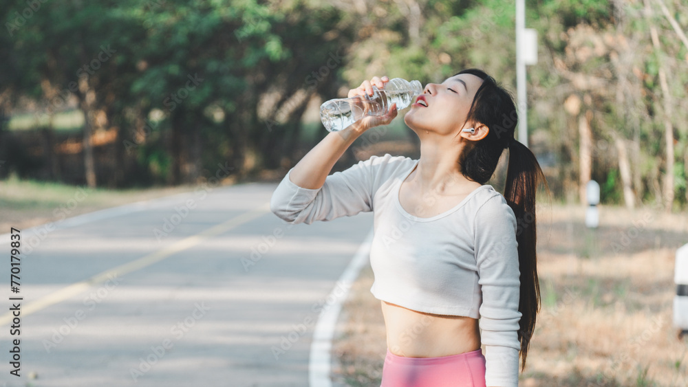 Young female athlete drinking water from a bottle after a workout, refreshing herself in a natural park setting.