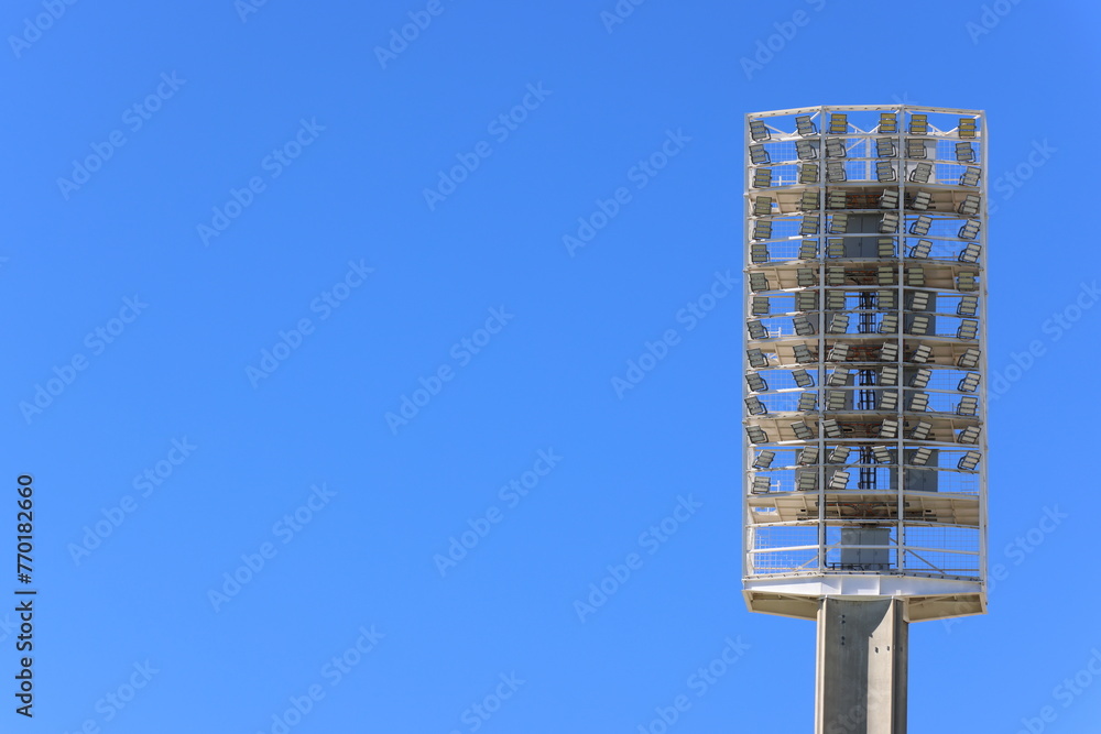 Light-emitting diode (LED) light tower, or floodlights, at large sports stadium or venue. Clear blue sky background. Copy space to left. Light-emitting diode (LED) light tower, or floodlights, at large sports stadium or venue. Clear blue sky background. Copy space to left.