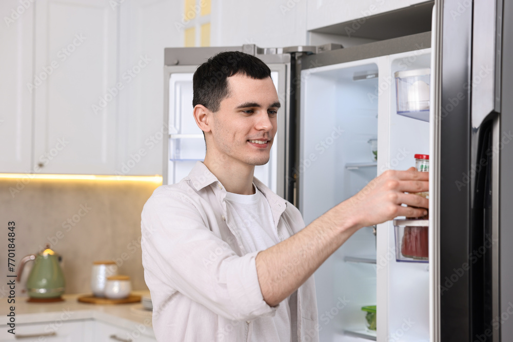 Happy man taking sauce out of refrigerator in kitchen
