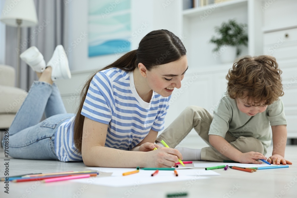 Mother and her little son drawing with colorful markers on floor at home Mother and her little son drawing with colorful markers on floor at home