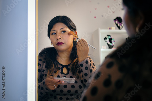 latina woman putting make-up powder with a brush on her face - make-up concept