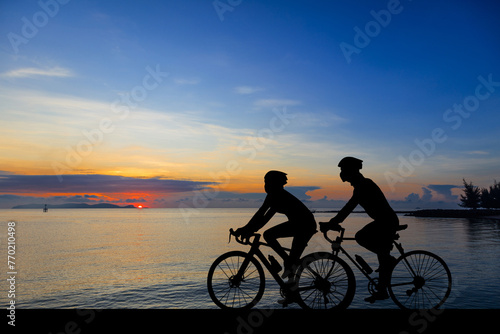 A silhouette of a cyclist on a mountain bike riding in a dramatic sunset background path.