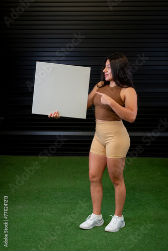 A standing female athlete holds a white board with her hands while pointing at it.