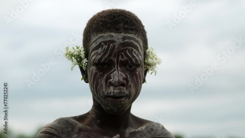 Closeup of A Kid with Face Paint from Karo Tribe with a flower on his ear