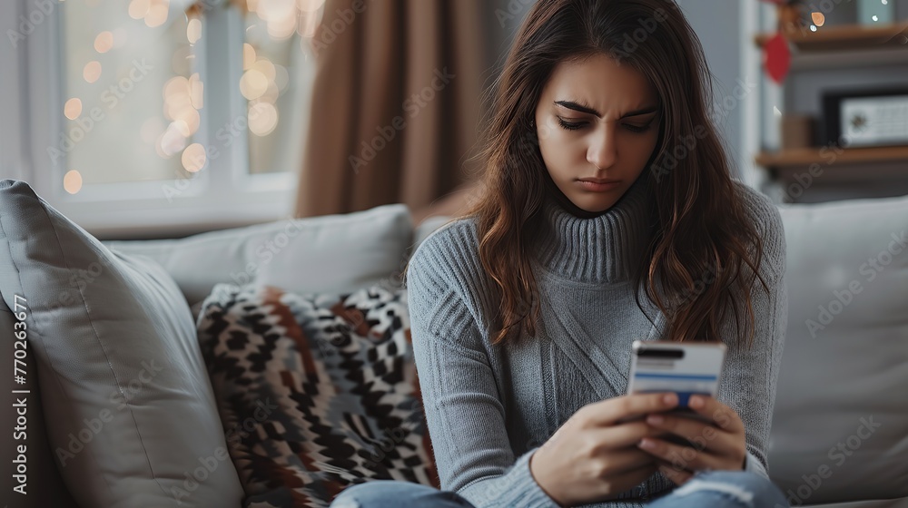Upset latina female internet shopper sit on couch hold phone with opened web shop ebank page suffer of overspending money from card account. Frustrated young lady lost savings. Upset latina female internet shopper sit on couch hold phone with opened web shop ebank page suffer of overspending money from card account. Frustrated young lady lost savings.