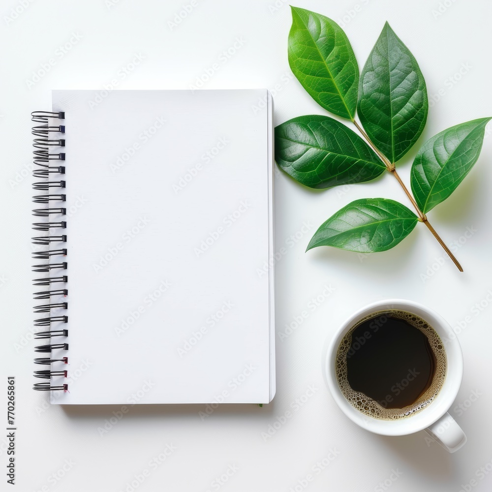 flat lay photograph showcasing blank white spiral notebook resting on table adorned with coffee cups and verdant green leaves, against minimalist white background. flat lay photograph showcasing blank white spiral notebook resting on table adorned with coffee cups and verdant green leaves, against minimalist white background.