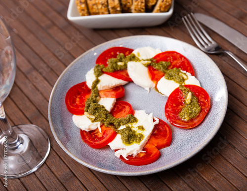 Fresh caprese salad with mozzarella, tomatoes and pesto sauce on plate