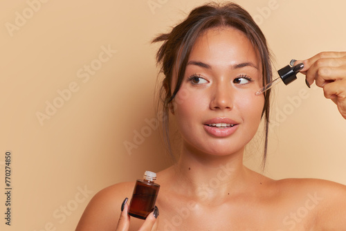 A woman applies serum with a pipette to her cheek and jaw