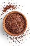 A bowl of brown seeds is on a white surface. The bowl is full of seeds and there is a lot of them on the surface