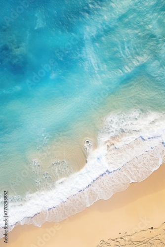 The ocean is calm and blue, with white foam on the shore. The water is a deep blue color, and the waves are small and gentle. The beach is sandy and stretches out into the distance. The sky is clear
