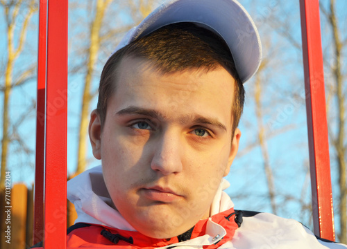Autistic guy in white cap swinging on swing in park in spring