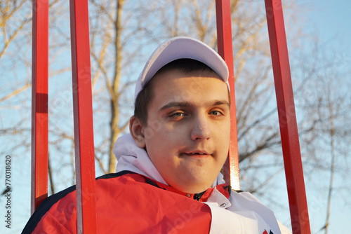 Young autistic guy on a walk in the park swinging on a swing