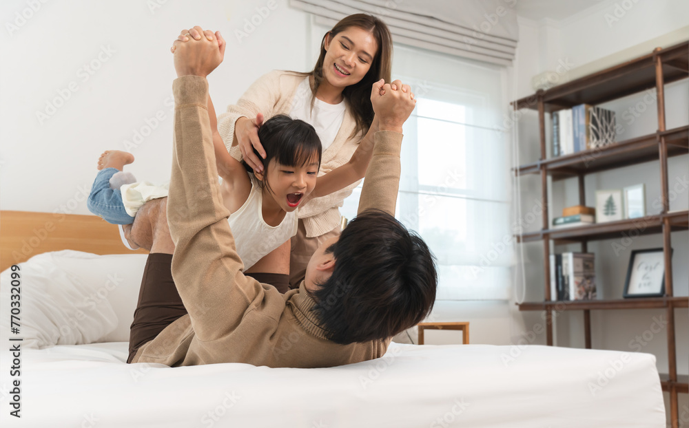 Happy Asian family, father, mother, cute daughter playing on bed in bedroom at home, bond and relax together. Little girl having fun playing be a plane on her dad smiling with happiness