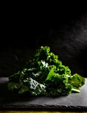 Curly leaves of kale piled on a dark slate board, with edges highlighted by the ambient light, emphasizing the rich green texture.