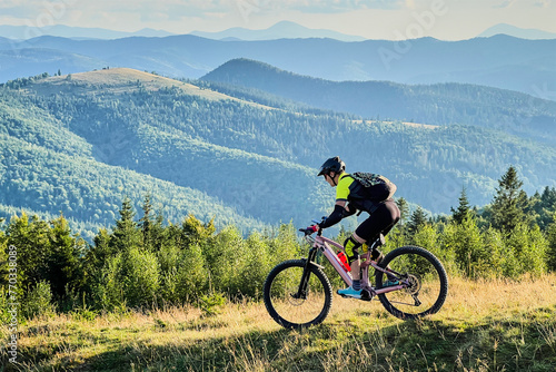 Cyclist man riding electric mountain bike outdoors. Male tourist biking along grassy trail in the mountains, wearing helmet and backpack. Concept of sport, active leisure and nature.