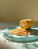 A cob of corn with kernels freshly cut, gathering in a golden heap on a ceramic board, showcasing the brightness and sweetness.