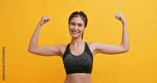 Young sportswoman shows physical strength. Isolated on yellow background in studio.