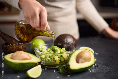 Woman pouring olive oil onto Chopped avocado in glass bowl and avocado Halves