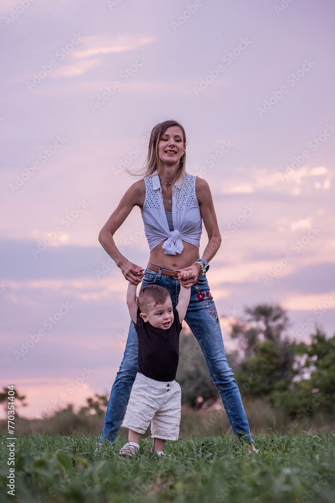 Woman lifts giggling toddler boy high in air against backdrop of soft purple sunset sky, moment of pure joy. Mother and little son playing on green meadow. Exuberant Mother and Child Playing at Sunset Woman lifts giggling toddler boy high in air against backdrop of soft purple sunset sky, moment of pure joy. Mother and little son playing on green meadow. Exuberant Mother and Child Playing at Sunset