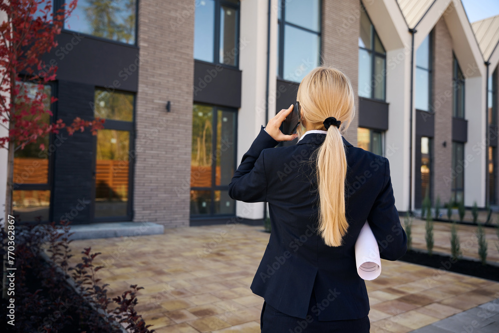 Fototapeta premium Female architect standing and talking on phone near houses