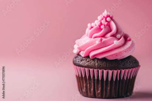 A delightful chocolate cupcake with pink frosting and sprinkles rests on a pink background photo