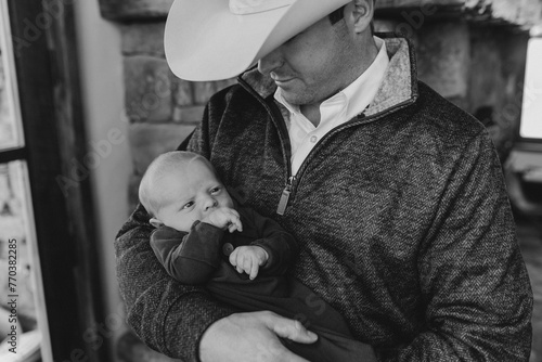 Dad in cowboy hat holds newborn son, smiling joyfully photo