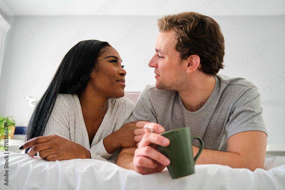 Multiethnic couple looking at each other and smiling in bed. Multiethnic couple looking at each other and smiling in bed.