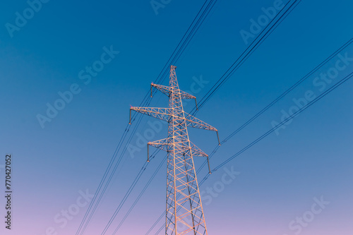 A tall power tower with many wires coming out of it. The sky is blue and clear. The tower is the tallest object in the image
