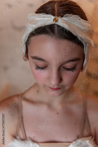 Close-up portrait of young ballerina in contemplative state, adorned with a delicate feather headpiece, captures the essence of youthful grace and the spirit of ballet.
