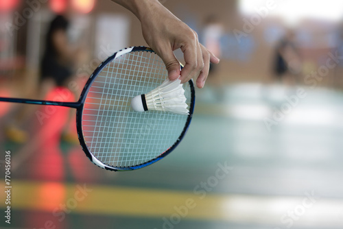 Badminton player holds racket and white cream shuttlecock in front of the net before serving it to another side of the court.  © Sophon_Nawit