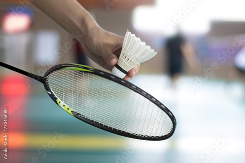 Badminton player holds racket and white cream shuttlecock in front of the net before serving it to another side of the court.	
