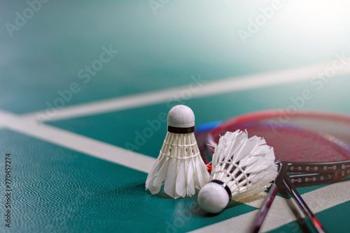 Cream white badminton shuttlecock and racket with neon light shading on green floor in indoor badminton court, blurred badminton court background, copy space.	