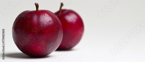   Two red apples on a white surface with a droplet of water