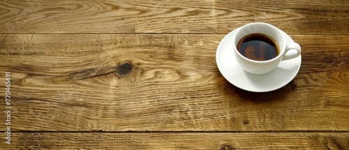  A cup of coffee sits on a saucer atop a wooden table alongside a spoon and a spoon rests atop the saucer