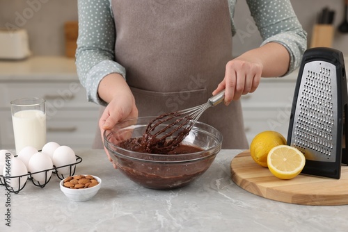 Woman mixing chocolate cream with whisk in bowl at gray marble table indoors, closeup