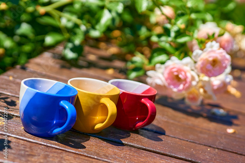 Tea time. Coffee break. Blue red yellow cups on wooden in blooming garden