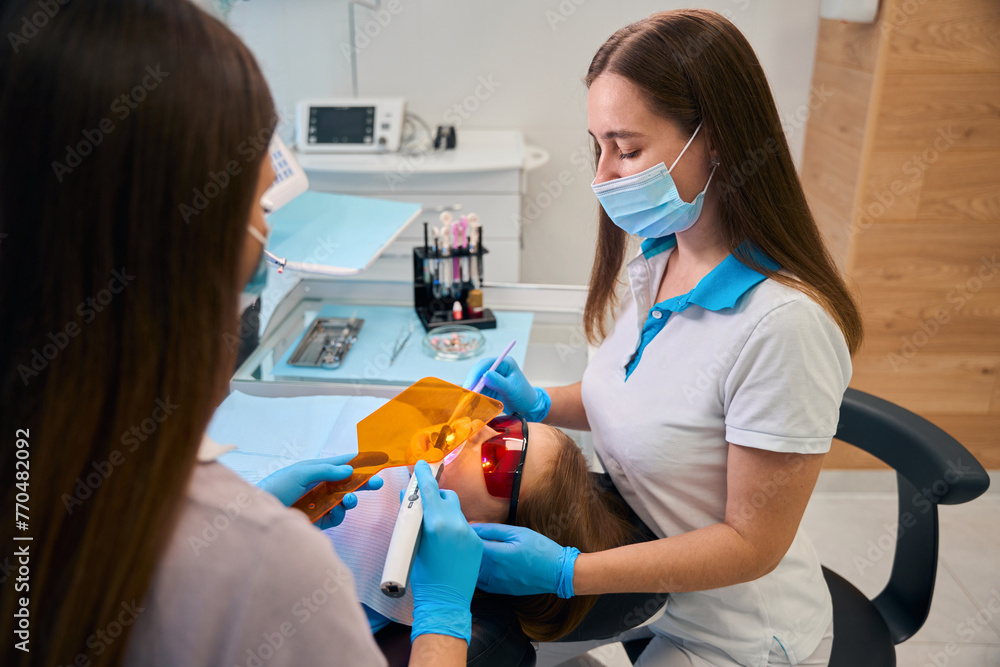 Dentist puts a photopolymer filling on a girl Dentist puts a photopolymer filling on a girl