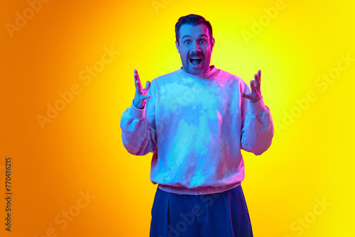 Positive excitement, news and sales ads. Man standing with smile speeding hands in joy on gradient yellow orange background in neon light. Success, win. Concept of human emotions, casual fashion