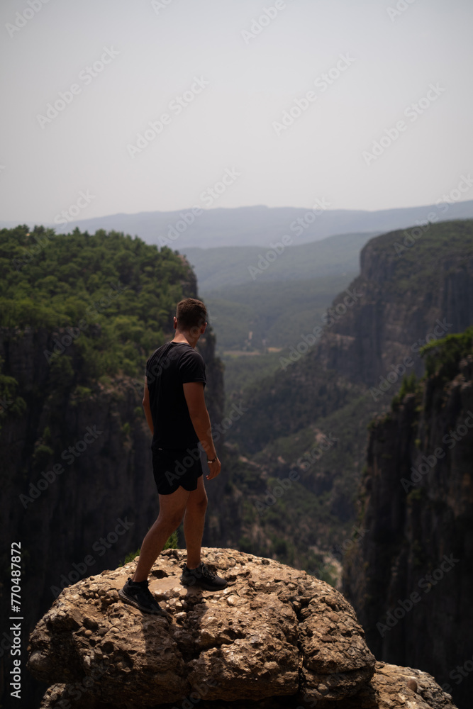 Man enjoys canyon amid green rocky mountains. Perfect for adventure tours, expeditions, and mountain excursions organized by travel agencies. Promotes mountain resorts and ski resorts.