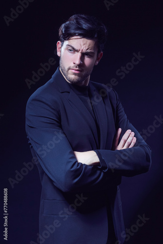 Portrait of Handsome Caucasian Brunet Businessman Wearing Black Suit Posing With Folded Hands Looking Aside Against Black