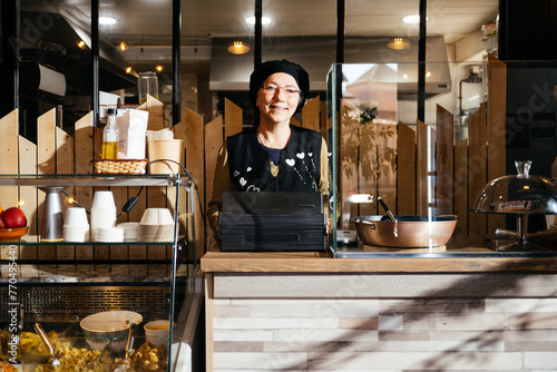 Smiling Woman Worker Poses Behind Counter in a Take Away Food Shop Looking at Camera