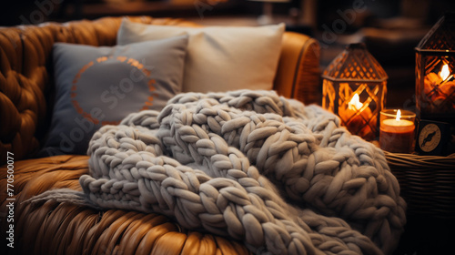 A cozy blanket made of chunky yarn on a brown leather sofa next to a lantern with a burning candle photo