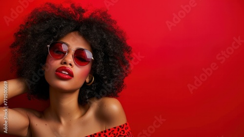 Stylish and confident Afro American woman poses with sunglasses against a vibrant red background, exuding an aura of beauty and charisma.
