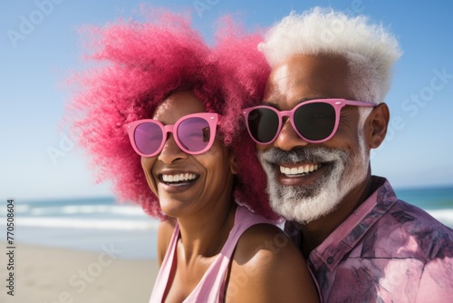 Elderly couple with vibrant pink hair and sunglasses on the beach.