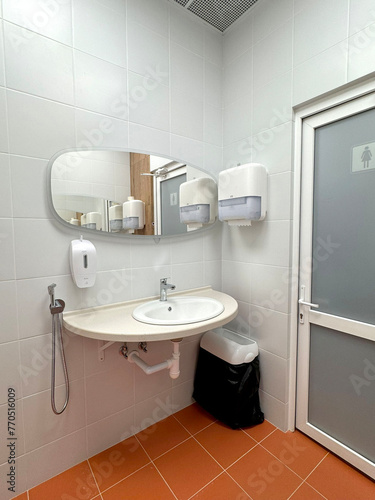 single sink in small public toilet with wall soap dispenser and paper towlels
